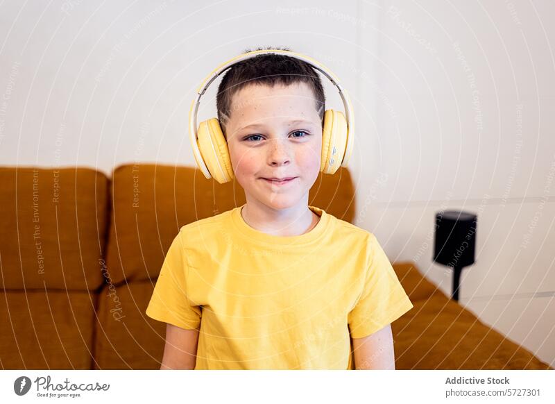 Lächelnder Junge mit gelben Kopfhörern zu Hause Kind T-Shirt heimwärts hören Musik Audio Entertainment Freizeit Technik & Technologie Youngster Glück lässig