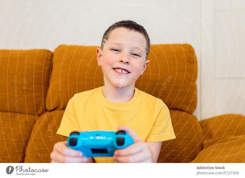 Glückliches Kind spielt Videospiele auf der Couch Spiel Regler Lächeln Junge spielen Liege Sitzen Freizeit im Innenbereich Freude blau Technik & Technologie