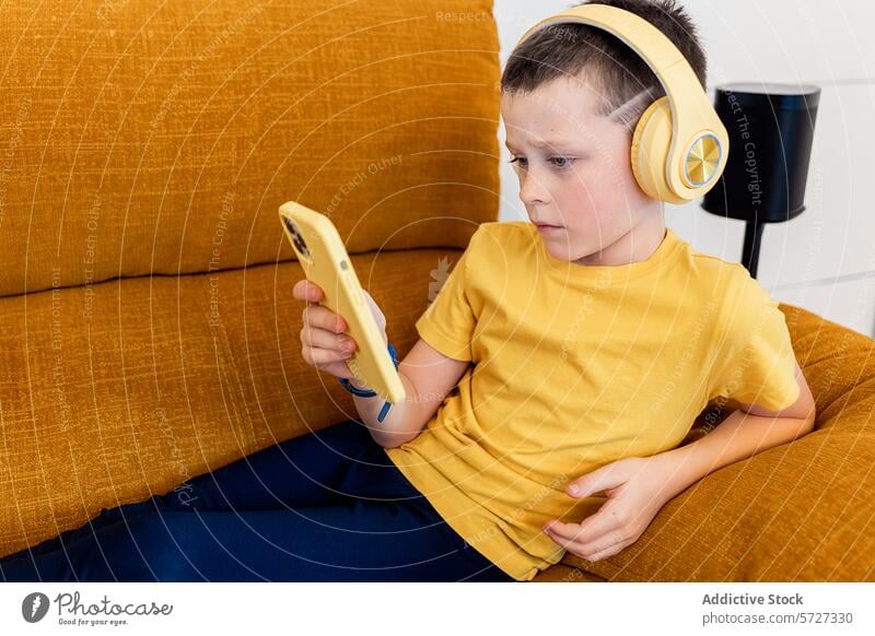 Kleiner Junge mit Kopfhörern, der sich zu Hause auf sein Smartphone konzentriert Liege jung fokussiert Sitzen Technik & Technologie Kind digital Bildschirmzeit