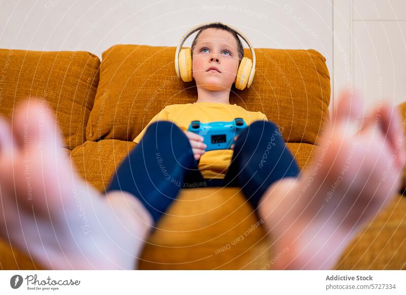Junge, der mit Kopfhörern in ein Videospiel vertieft ist Spielen fokussiert Liege Regler engagiert jung Sitzen braun gelb blau Gamepad Entertainment