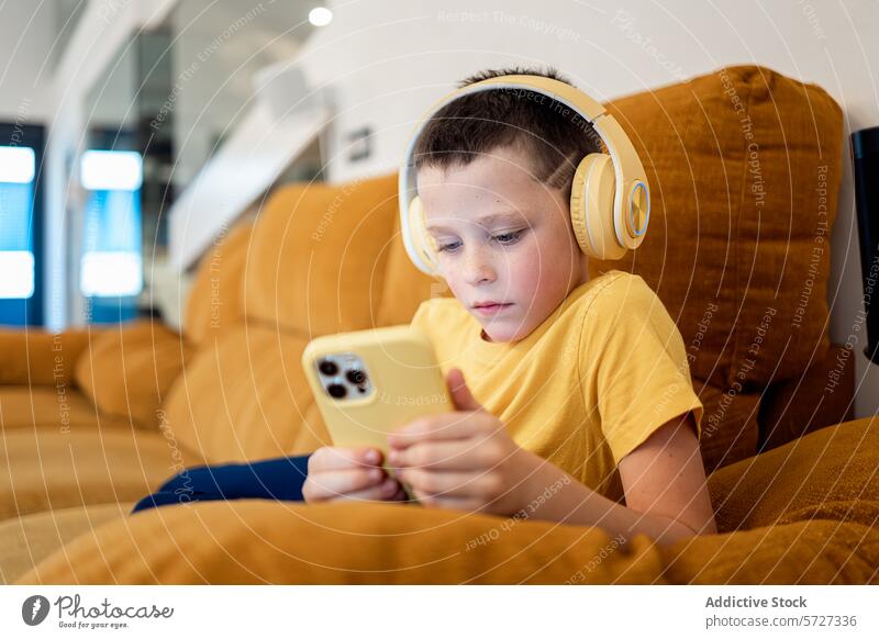 Junge, der mit Kopfhörern in sein Smartphone vertieft ist Liege Senf konzentriert engagiert gelb Sitzen Technik & Technologie Bildschirm digital Gerät Mobile