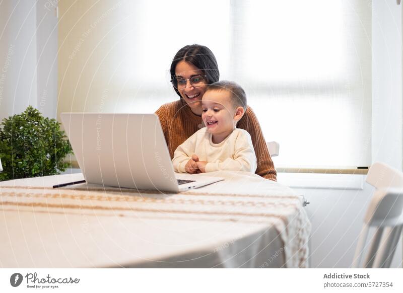 Ein herzerwärmender Moment, als eine lächelnde Mutter ihren Sohn umarmt, während sie beide zu Hause auf einem Laptop Inhalte bearbeiten Umarmen Lächeln