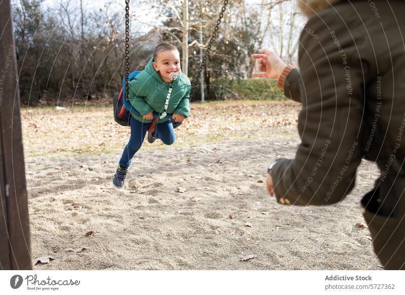 Ein spielerischer Moment, der eingefangen wurde, als ein kleines Kind kichert, während es sich in einem sonnigen Park in Richtung einer ausgestreckten anonymen Hand schwingt