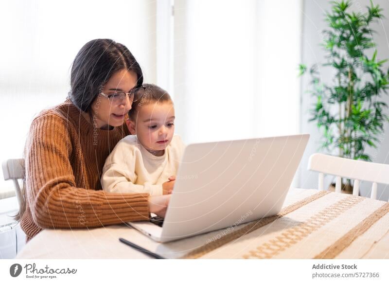 Ein herzerwärmender Moment, in dem eine positiv gestimmte Mutter ihren Sohn umarmt, während sie beide zu Hause auf einem Laptop mit Inhalten arbeiten Umarmen