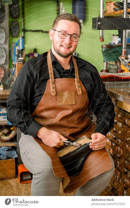 Ein gelernter Schuhmacher bei der Arbeit in seiner Werkstatt in Österreich Schuster Handwerkskunst Reparatur Fähigkeit jung heiter Experte professionell Schürze