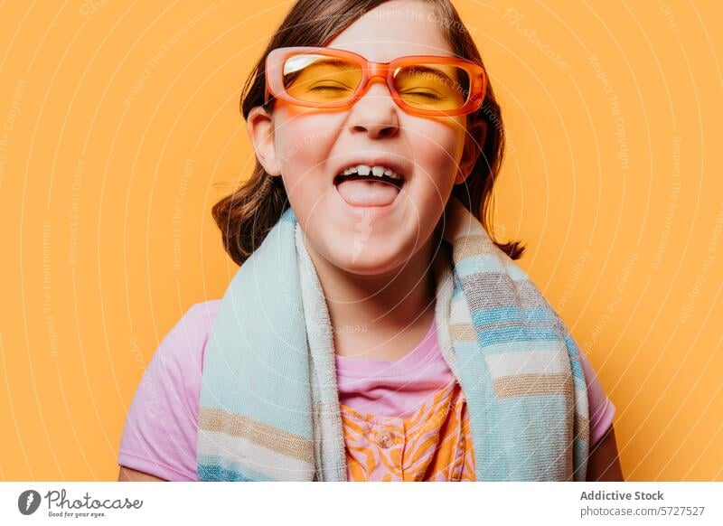 Glückliches Kind mit bunter Brille, die die Zunge herausstreckt Mädchen heiter orange farbenfroh Spaß hell Hintergrund Freude spielerisch Jugend Kinder Ausdruck