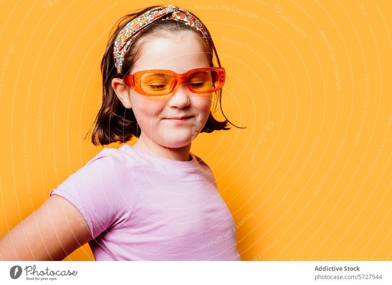 Lächelndes Kind mit buntem Stirnband und Sonnenbrille Mädchen spielerisch trendy orange Hintergrund heiter jung Mode farbenfroh Stil Fröhlichkeit Brille Porträt