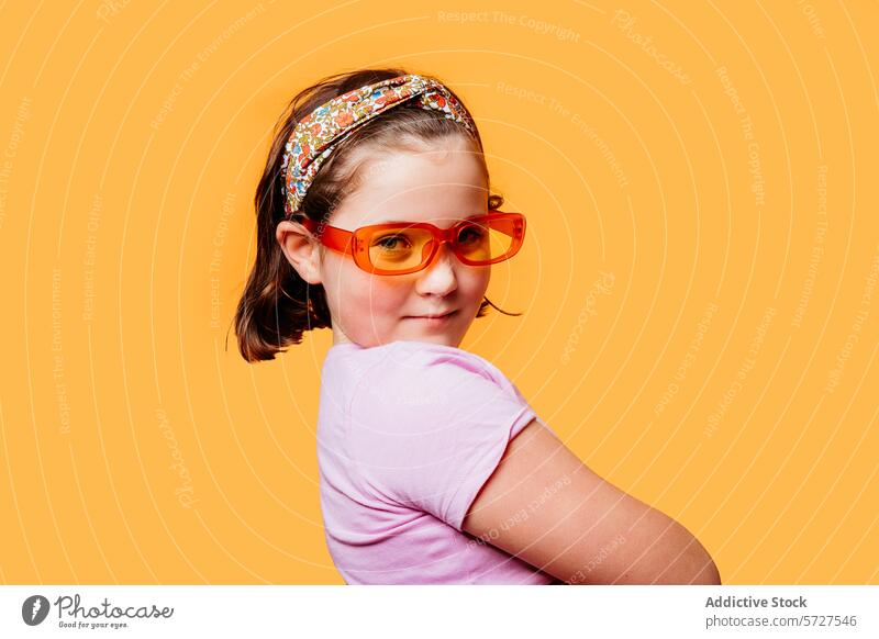 Junges Mädchen mit modischer Sonnenbrille auf orangefarbenem Hintergrund jung Kind niedlich Stirnband Selbstvertrauen Pose spielerisch heiter Mode stylisch
