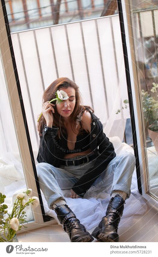 schöne Frau in Grunge-Outfit mit weißer Blume sitzt auf dem Balkon der Wohnung 25 bis 30 Jahre Junge Frau Grunge-Look Bekleidung Outfits Sitzen Stil Mode