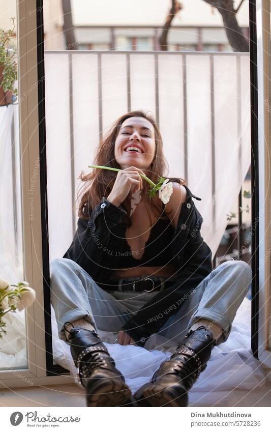 schöne Frau lächelnd in Grunge-Outfit mit weißer Blume sitzt auf dem Balkon der Wohnung 25 bis 30 Jahre Junge Frau Grunge-Look Bekleidung Outfits Sitzen Stil