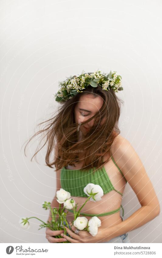 schöne Frau in grün häkeln handgefertigte Top mit weißen Blumen und Blumen Stirnband auf weißen Wand minimal Hintergrund jung Frühling Porträt eine Mädchen
