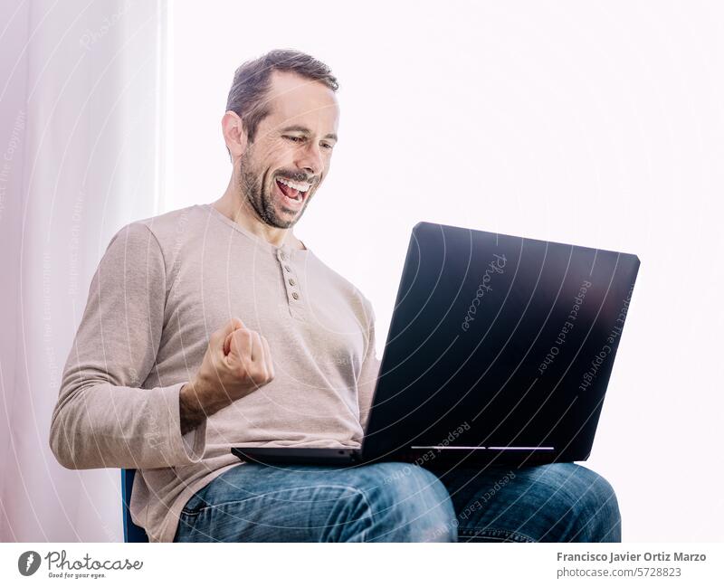 Mann schaut auf seinen Laptop, glücklich über den Erfolg seiner Arbeit Glück aufgeregt Kaukasier Person Hemd Feier blau Erwachsener Computer arbeiten Internet