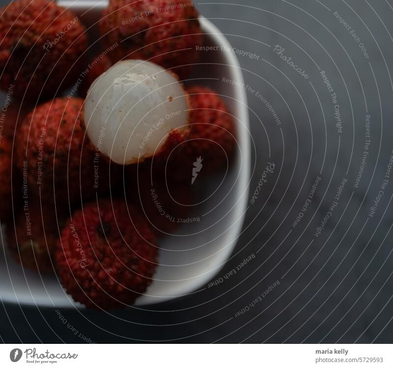 Das Bild zeigt einen Teller mit Lebensmitteln, die Litschi-Früchte enthalten. Es handelt sich um eine Innenaufnahme mit roten Früchten auf dem Teller. stachelig