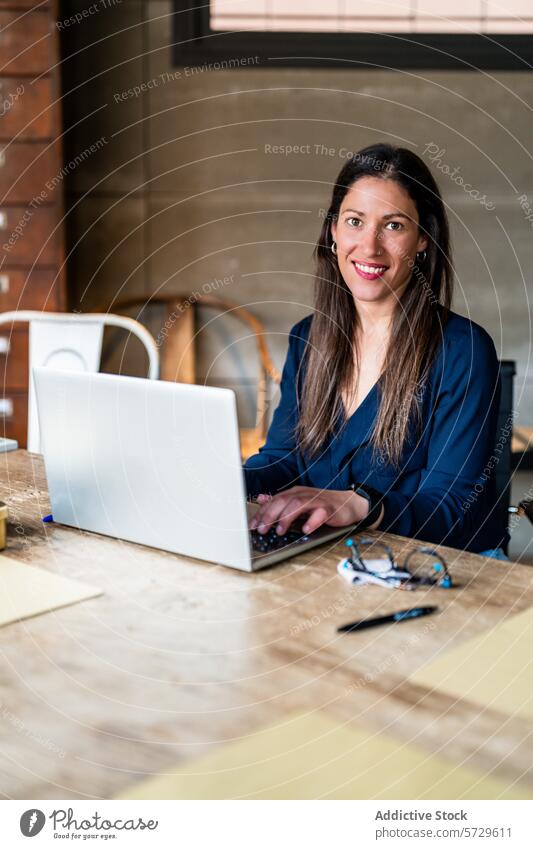 Unternehmerin arbeitet am Laptop am Schreibtisch Frau arbeiten Lächeln in die Kamera schauen Business Büro selbstbewusst professionell freundlich Holztisch