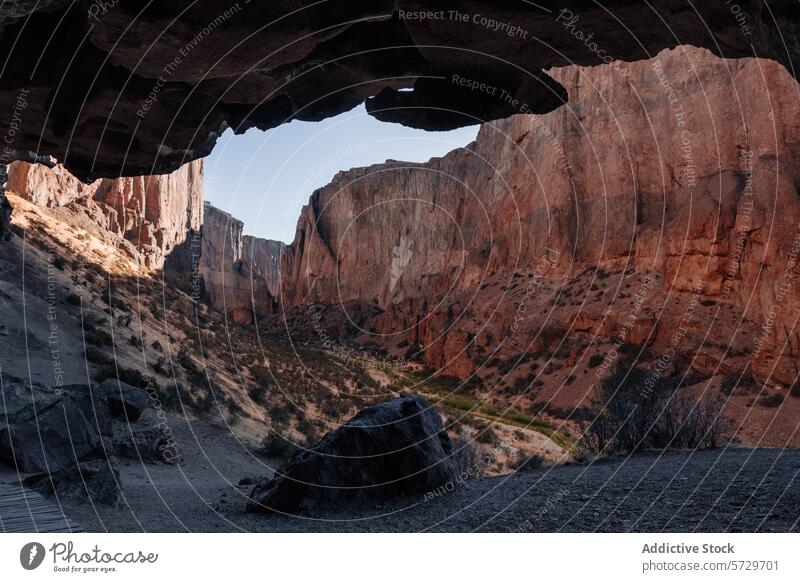 Blick aus dem schattigen Inneren einer Höhle auf die sonnenbeschienenen roten Felsen eines patagonischen Canyons, der ein Gefühl von abgelegener Wildnis hervorruft