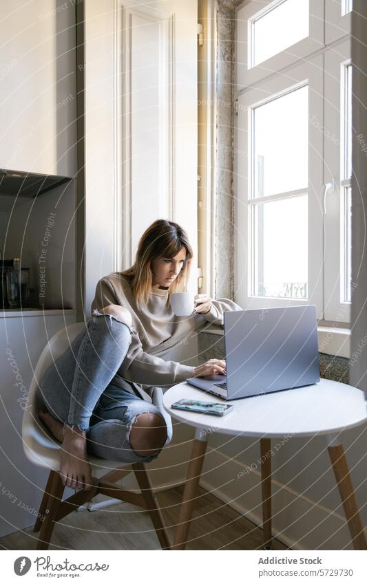 Junge Frau arbeitet von zu Hause aus an einem Laptop arbeiten heimwärts Fenster Kaffee Tasse sitzend Raum Licht Technik & Technologie Fernarbeit freiberuflich