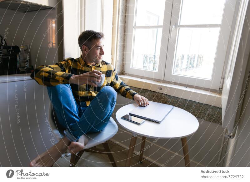 Nachdenklicher Mann mit Kaffee und Blick aus dem Fenster Kontemplation Pause Tisch Sitzen kariertes Hemd Beteiligung Becher geschlossener Laptop Smartphone
