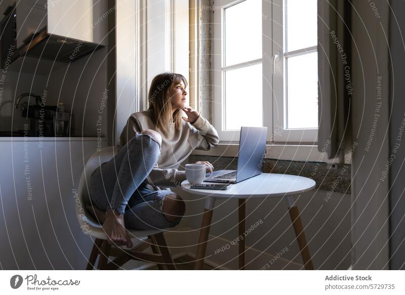 Nachdenkliche Frau bei der Arbeit von zu Hause am Fenster Laptop Denken Kaffee heimwärts abgelegen Kontemplation sonnenbeschienen Tisch Stuhl im Innenbereich