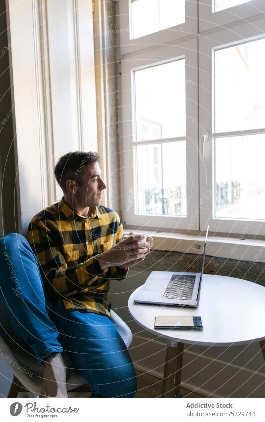 Mann entspannt sich mit Kaffee und Laptop am Fenster Tisch entspannend Sitzen kariertes Hemd Getränk Becher im Innenbereich lässig Technik & Technologie