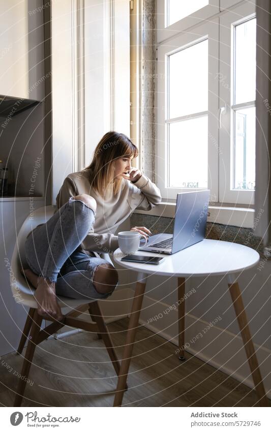 Junge Frau arbeitet zu Hause am Laptop mit Kaffee Tisch heimwärts arbeiten jung sitzend Fenster Fokus Computer Tasse runder Tisch weißer Tisch Heimarbeitsplatz
