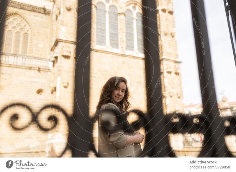 Eine Frau wirft einen sanften Blick durch ein verziertes schmiedeeisernes Tor mit der historischen Fassade einer Kathedrale im Hintergrund Starrer Blick