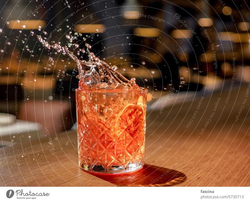 Rotbrauner Cocktail mit Wasserspritzern in einem Nachtclub Geplätscher weltoffen platschen Alkohol rot orange negroni Glas trinken Tropfen Getränk Blutorange