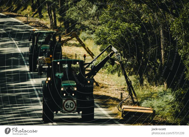 Traktoren mit Mähwerk tätig am Straßenrand Sonnenlicht Schatten roadtrip zweispurig Mittelstreifen unterwegs Roadmovie Landstraße Verkehrswege außerorts