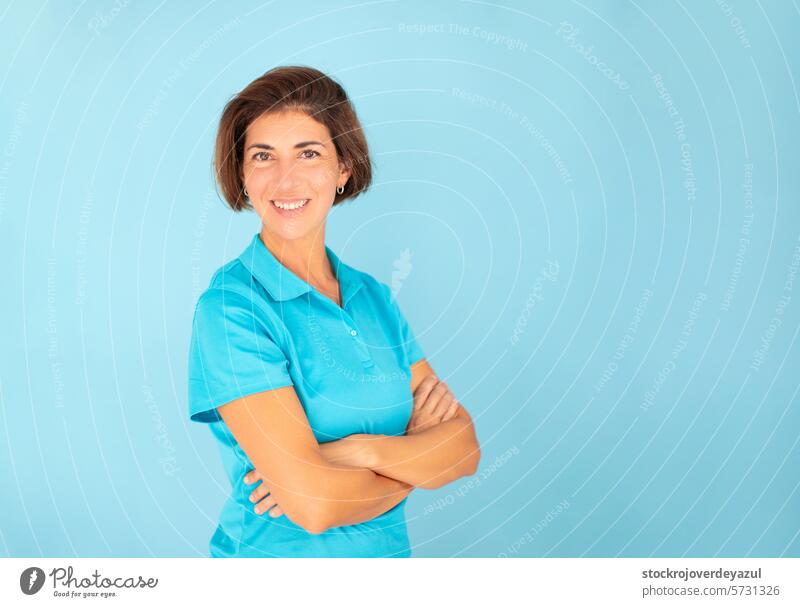 Eine Frau, eine Physiotherapeutin, posiert mit einer zuversichtlichen Geste, blickt in die Kamera auf einem blauen Hintergrund und trägt ein blaues T-Shirt.