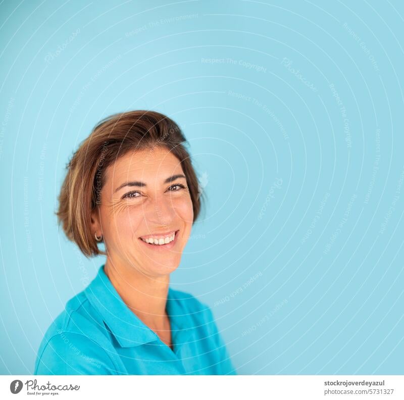 Eine Frau, Inhaberin einer eigenen Physiotherapiepraxis, lächelt selbstbewusst auf einem einfarbig blauen Hintergrund. Physiotherapeutin Frauen Porträt Lächeln