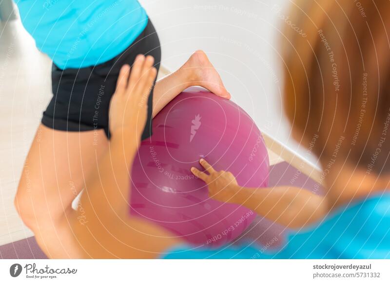 Eine Physiotherapeutin hilft einem Patienten bei einer Übung mit einem Fitnessball in einer therapeutischen Pilates-Trainingseinheit Fitball Ball Klinik