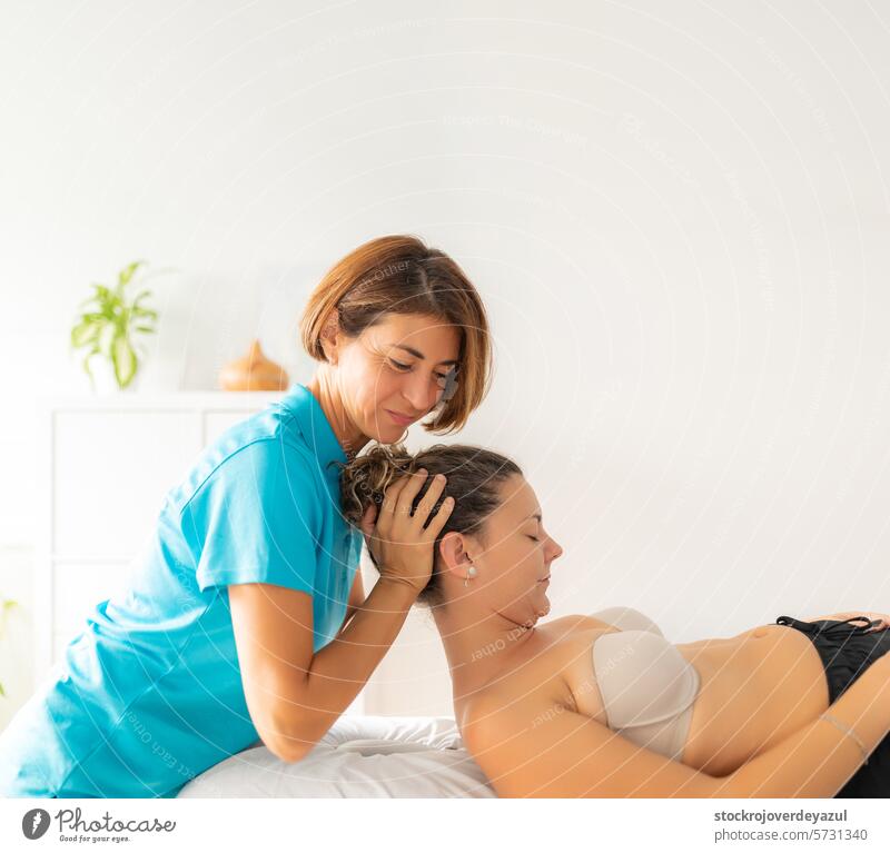 Eine Physiotherapeutin führt eine Dehnungsübung am Nacken ihres Patienten durch, der entspannt auf der Liege liegt. Klinik Rehabilitation geduldig