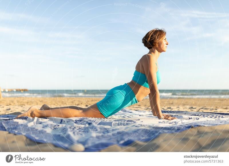 Eine Frau praktiziert Pilates am Strand und führt die Schwanenbewegung aus Übung Yoga mediterran Spanien Körper-Geist-Übung Kontrolleogie Sonnenuntergang