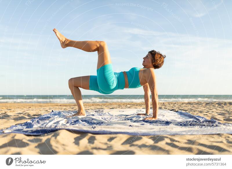Eine Frau macht Pilates-Übungen am Strand und führt eine Beinrückzugsbewegung aus Yoga mediterran Spanien Körper-Geist-Übung Kontrolleogie Sonnenuntergang Sport