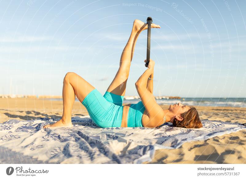 Eine Frau führt am Strand Pilates-Übungen mit einem Pilates-Ring durch, um die Beine zu dehnen Yoga mediterran Spanien Körper-Geist-Übung Kontrolleogie