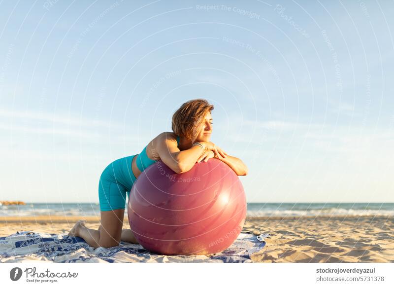 Eine Frau ruht sich aus und entspannt sich während einer Pilates-Sitzung am Strand, während sie sich auf einen Pilates-Ball stützt Übung mediterran Spanien