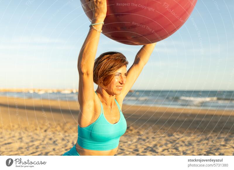 Eine Frau macht Dehnungs- und Gleichgewichtsübungen mit einem Pilates-Ball während einer Sitzung am Strand Übung mediterran Spanien Körper-Geist-Übung
