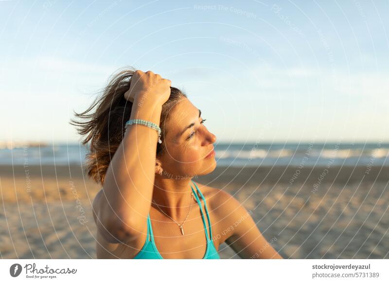 Eine Frau streichelt ihr Haar, während sie die letzten Sonnenstrahlen nach einer Pilates-Sitzung am Strand genießt Übung mediterran Spanien Körper-Geist-Übung