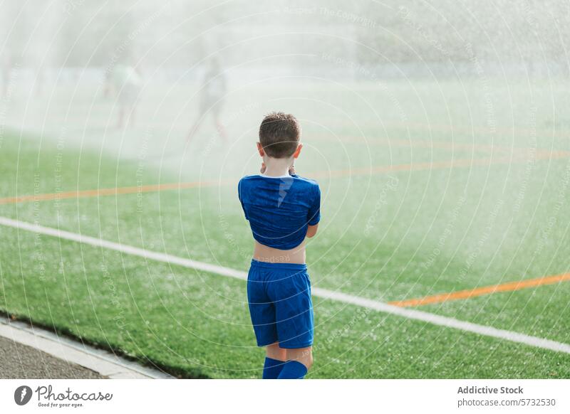 Junger Fußballspieler auf einem nebligen Feld während eines Sprinklerlaufs Sportbekleidung Wasser Sprinkleranlage Nebel Hintergrund jung Spieler Kind Jugend