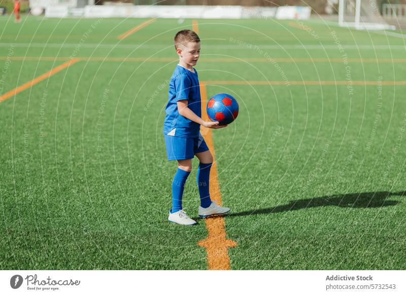 Junger Fußballspieler hält Ball auf dem Feld Spieler Sport Rasen künstlich grün Gras Selbstvertrauen spielen Uniform lässig Sportbekleidung im Freien sportlich
