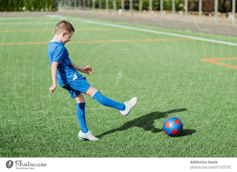 Junger Junge spielt Fußball auf einer grünen Wiese spielen Sport Feld Kunstrasen blaue Uniform Kick Ball Kind im Freien Aktivität Spiel Jugend Fußballfeld