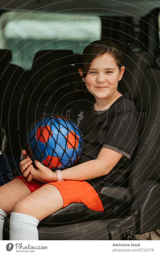Lächelndes Kind mit Ball im Auto sitzend Autositz Sicherheit Sport Fahrzeug Sicherheitsgurt reisen Mädchen Fröhlichkeit Jugend Aktivität Transport Freizeit