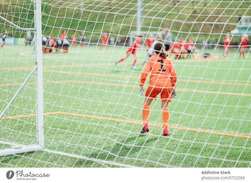 Junger Torwart, der während eines Fußballspiels im Tor wartet jung Spieler orange Uniform Handschuhe Streichholz grün Rasen Feld Sport Jugend künstlich