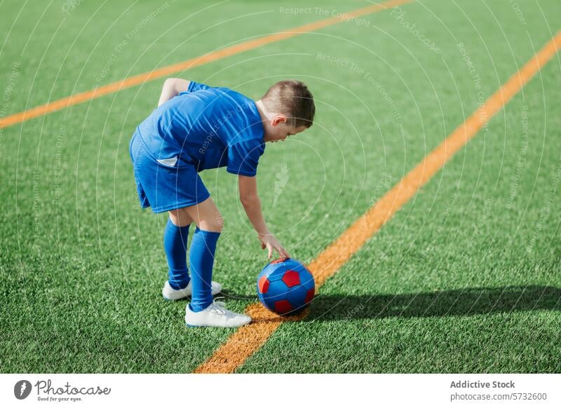 Junger Fußballspieler bereitet sich auf dem Spielfeld auf den Anstoß vor Spieler jung Athlet blau Uniform Biegungen Ball rot weiße Linie grün Kunstrasen Feld