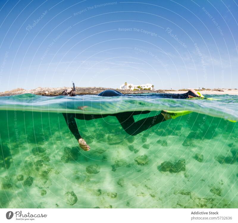 Anonyme Schnorchler durchqueren das klare türkisfarbene Wasser über einem felsigen Meeresgrund mit einem malerischen Küstenhintergrund felsiger Meeresboden