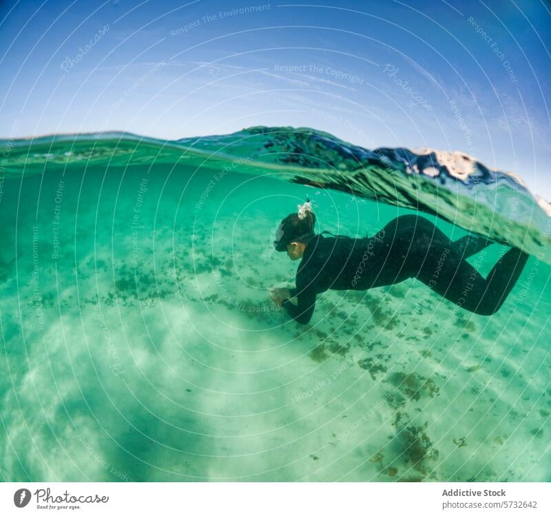 Ein Schnorchler wird in einem heiteren Moment festgehalten, wie er mühelos über einem sandigen Meeresgrund taucht, während die Wasseroberfläche die Sonnenstrahlen reflektiert