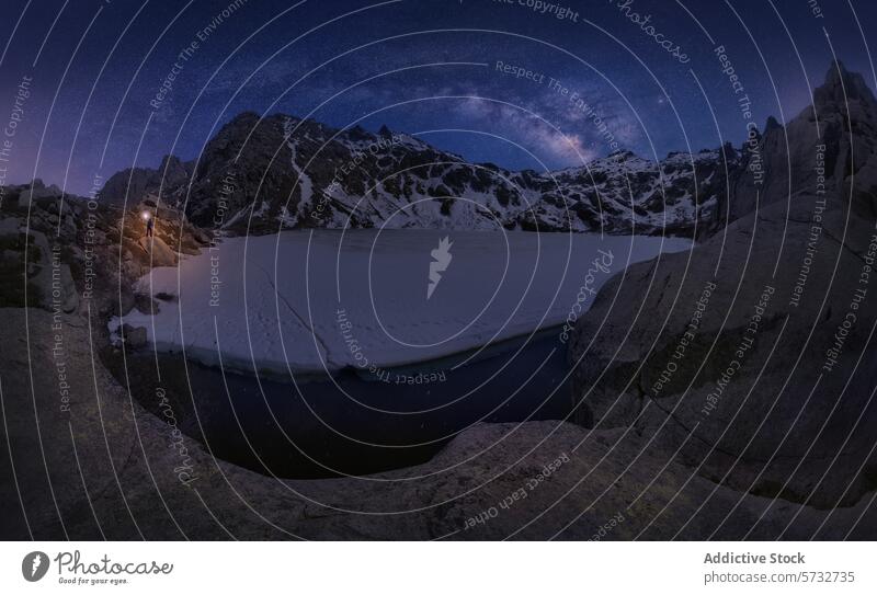 Ein majestätischer Sternenhimmel bedeckt einen zugefrorenen Bergsee in Korsika, Frankreich, und ein einsamer Wanderer beleuchtet die ruhige Szene