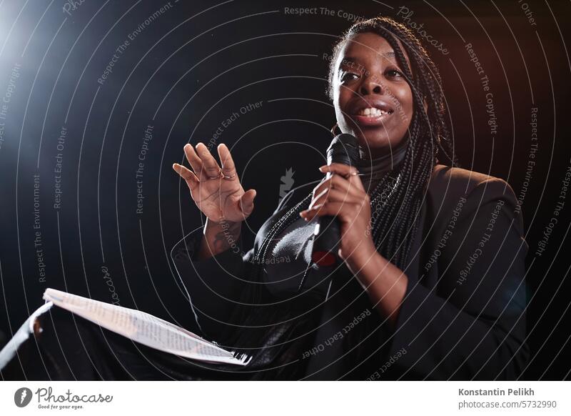 Porträt einer afroamerikanischen Frau, die ein Mikrofon hält und einen eleganten schwarzen Anzug trägt, während sie auf der Bühne spricht, Kopierraum