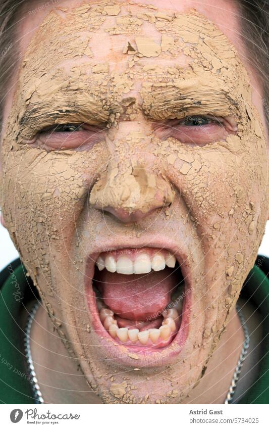 Ein schreiender Mann mit einer Maske aus Erde mann gesicht maske rufen heilerde schmutz schmutzig dreck dreckig trocken haut schmerz schmerzen pflege