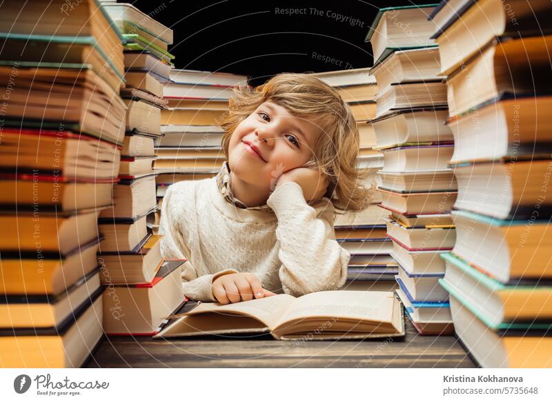 Verträumter kleiner Junge sitzt am Schreibtisch im Klassenzimmer oder in der Bibliothek. Smart Kind lächelnd, denken über Studie oder vielleicht Schulferien, Ende der Lektion