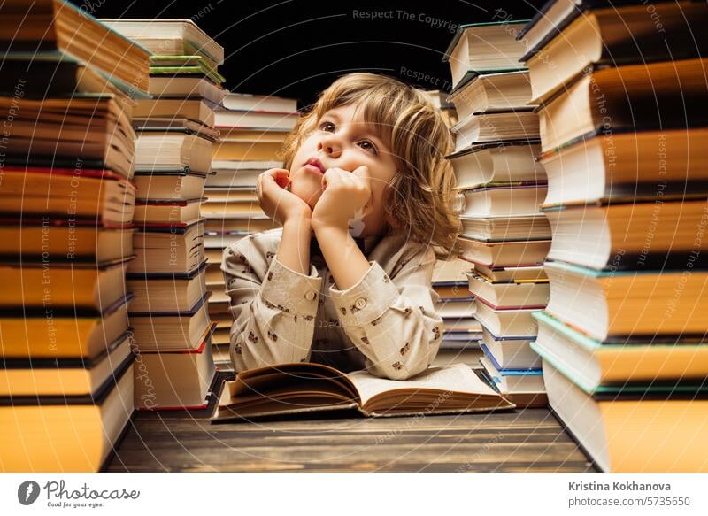 Verträumter kleiner Junge sitzt am Schreibtisch im Klassenzimmer oder in der Bibliothek. Smart Kind lächelnd, denken über Studie oder vielleicht Schulferien, Ende der Lektion